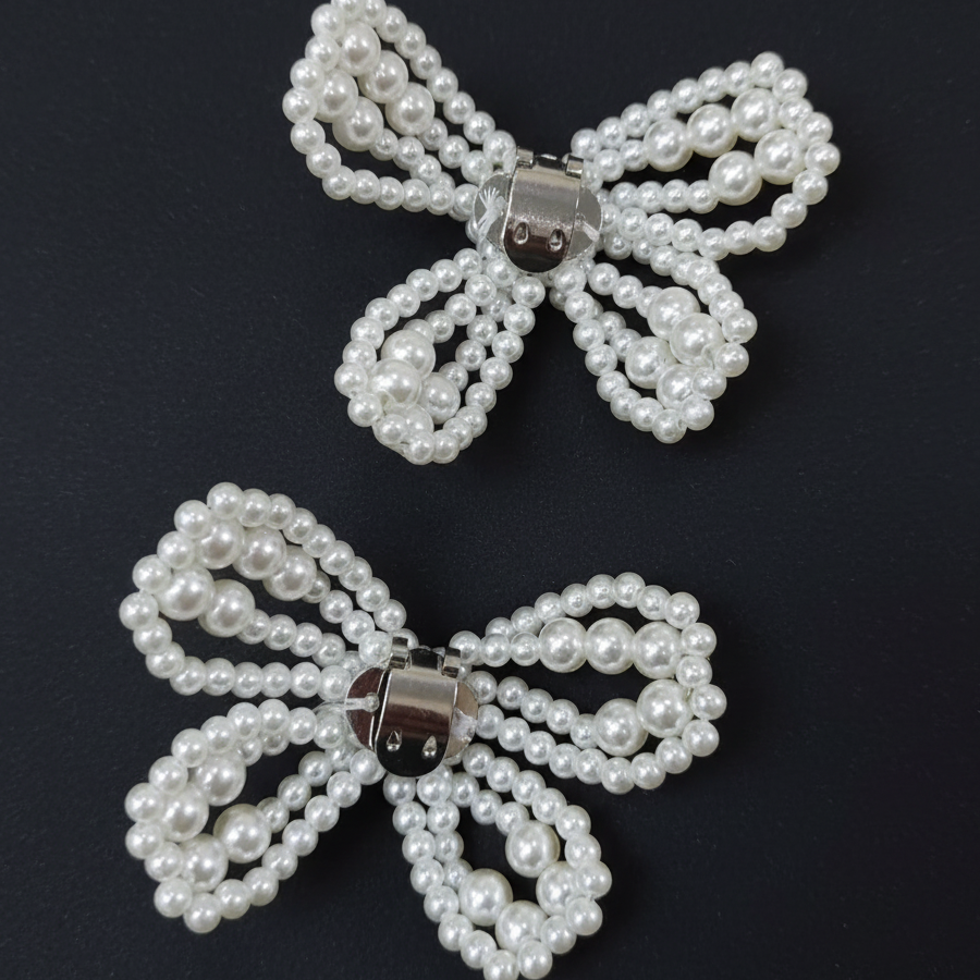 Two pearl-bead bow hair clips with silver metal clasps, displayed on a solid beige background.