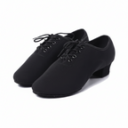 A pair of black dance shoes with a low block heel and lace-up front, shown on a white background with a circular inset detail of the fabric texture.