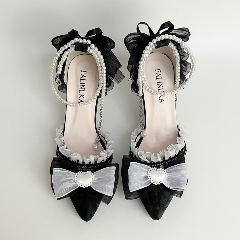 A pair of black and white bridal-style pointed-toe flats with ruffled trim, pearl bead straps, and large bow details, arranged on a white fabric surface with pink flowers and lace props. The insole shows the brand name FALINUKA.