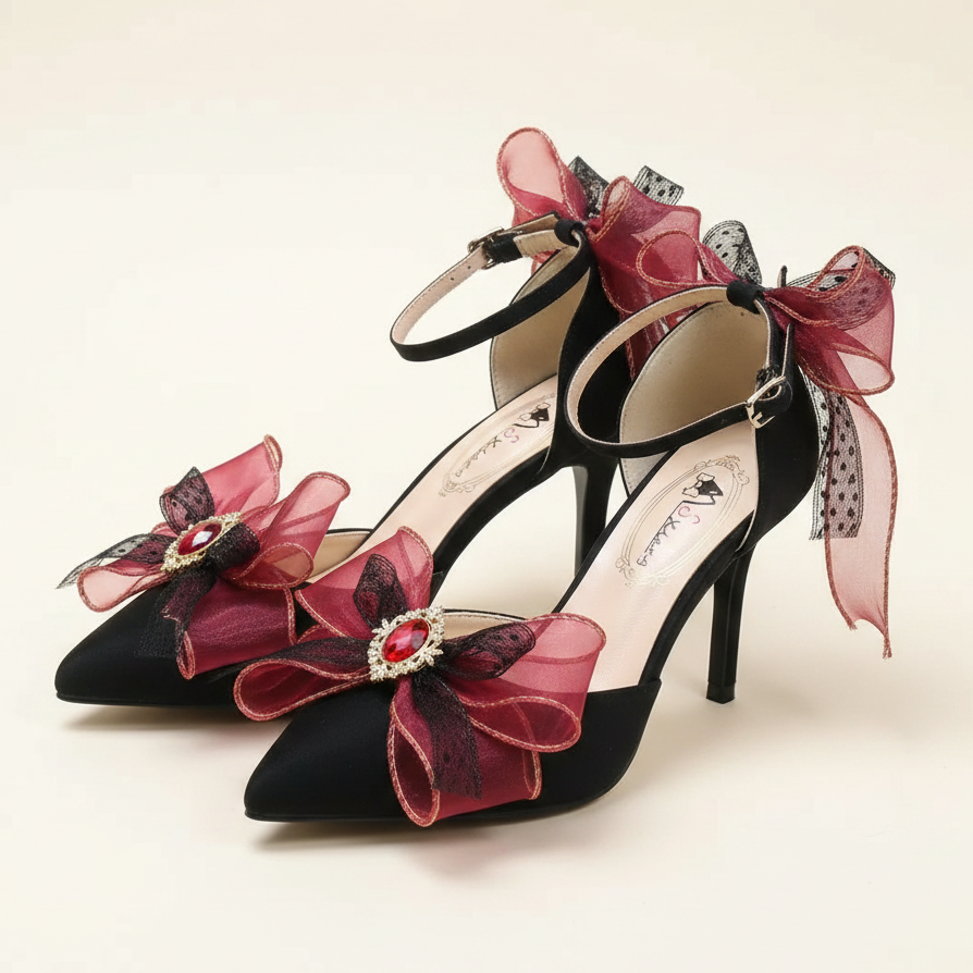A pair of pointed-toe high heels with dark red and burgundy ribbon bows, velvet detailing, and red crystal embellishments, shown on a reflective surface with a blurred background.