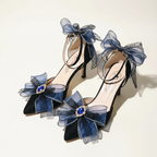 A pair of high-heeled Lolita-style shoes in dark blue velvet and navy blue mesh, decorated with large bows, blue rhinestone accents, and ankle straps, displayed on a reflective surface.