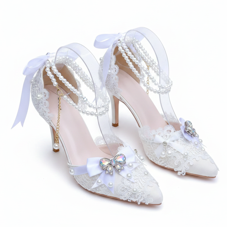 A pair of embellished high-heeled shoes displayed on a mirrored tray with pink flowers in the background. The shoes feature clear straps with pearl bead strands, pale lavender bows, white lace detailing, and iridescent butterfly embellishments on the toes.